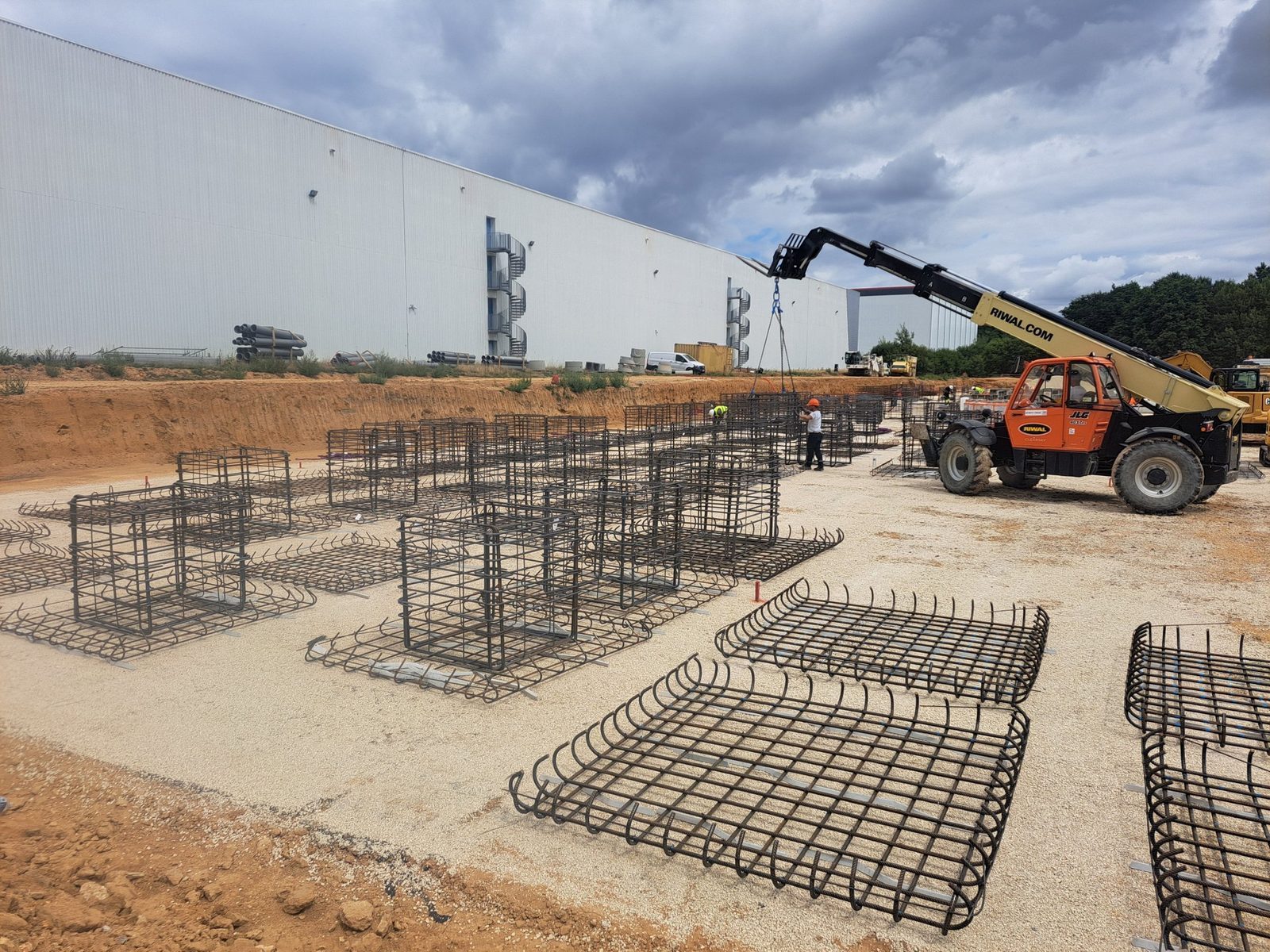 Cages d'armatures des massifs en place sur un chantier de bâtiment logistique, levage au chariot télescopique